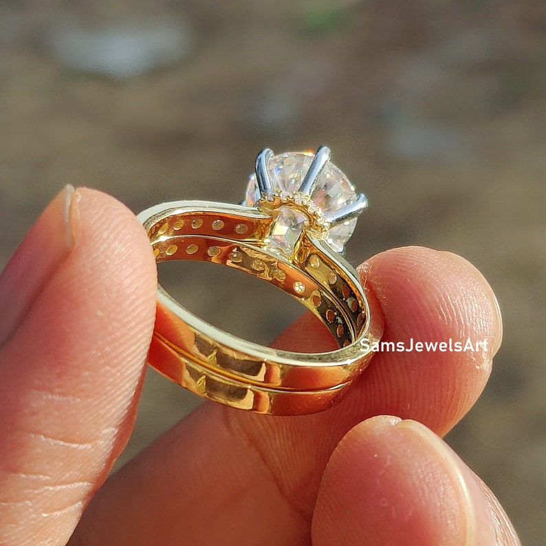 May include: A gold wedding band set with a large, round, clear center stone and a smaller band with a row of smaller clear stones.