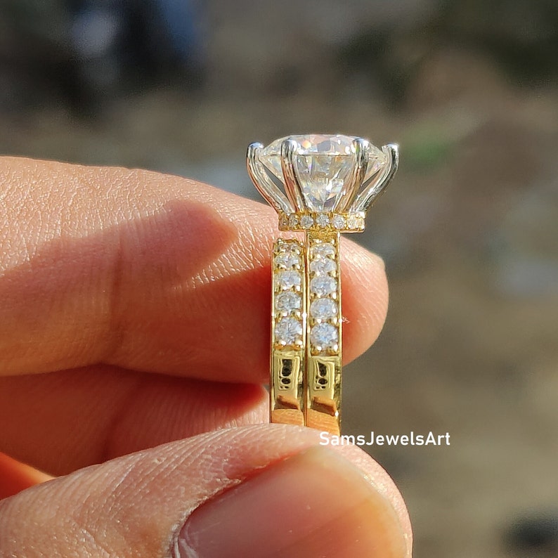 May include: A gold engagement ring set with a large, round, clear center stone and a halo of smaller stones. The band is also set with smaller stones. The ring is on a finger.