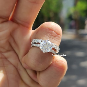 May include: A stunning engagement ring set with a large, round-cut diamond as the focal point. The band is embellished with smaller, sparkling stones, creating a dazzling effect. The ring is set in a silver or white gold setting.