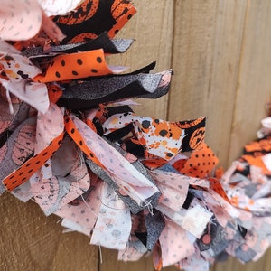 May include: A Halloween garland made of fabric scraps in black, orange, white, and gray with various patterns, including polka dots, pumpkins, and splattered paint.