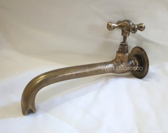 Puede incluir: Un grifo de latón de estilo vintage con un caño curvo y un mango en forma de cruz. El grifo tiene una base circular y el texto "WorksMorocco" es visible. El accesorio está hecho de latón metálico cálido.