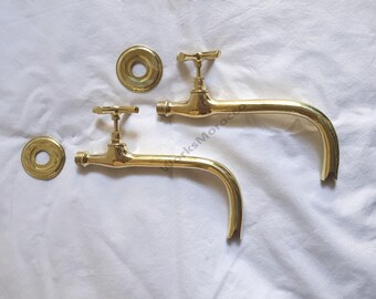 Puede incluir: Dos grifos de pared de latón pulido con caños largos y curvos y manijas en forma de T. Cada grifo incluye una placa de brida circular de latón a juego. El metal tiene un acabado dorado brillante y reflectante en todo el conjunto.