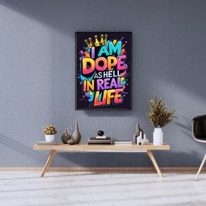 May include: A framed art print with the text "I AM DOPE AS HELL IN REAL LIFE" in vibrant colors. The artwork features a gold crown and colorful paint splatters against a dark background. The print is displayed on a light wood table.