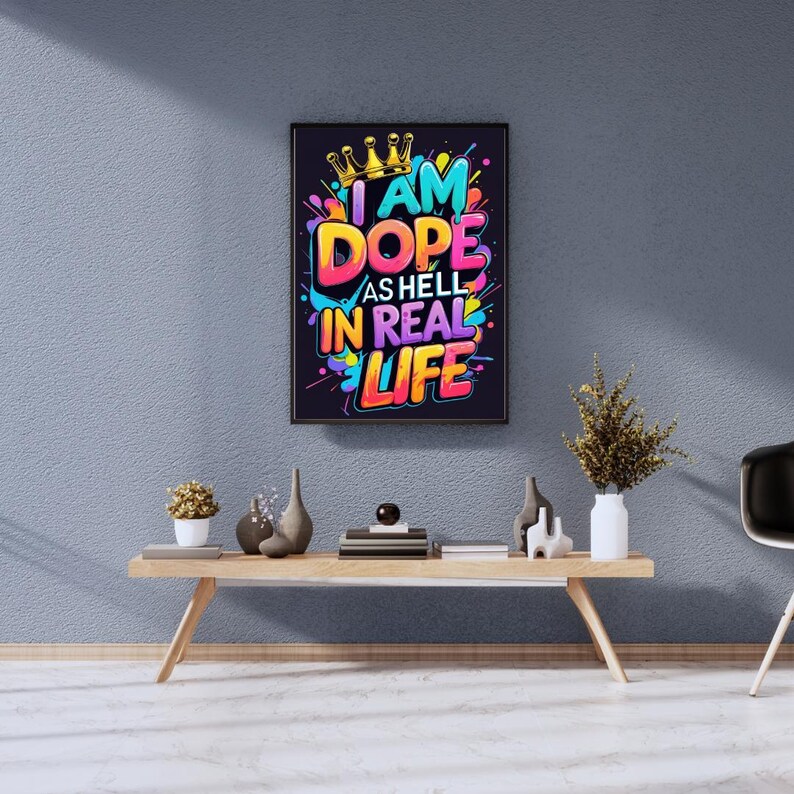May include: A framed art print with the text "I AM DOPE AS HELL IN REAL LIFE" in vibrant colors. The artwork features a gold crown and colorful paint splatters against a dark background. The print is displayed on a light wood table.