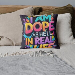 May include: A decorative throw pillow with the text "I AM DOPE AS HELL IN REAL LIFE" in vibrant colors. The pillow has a black background with colorful paint splatter accents, perfect for adding a pop of personality to any space.