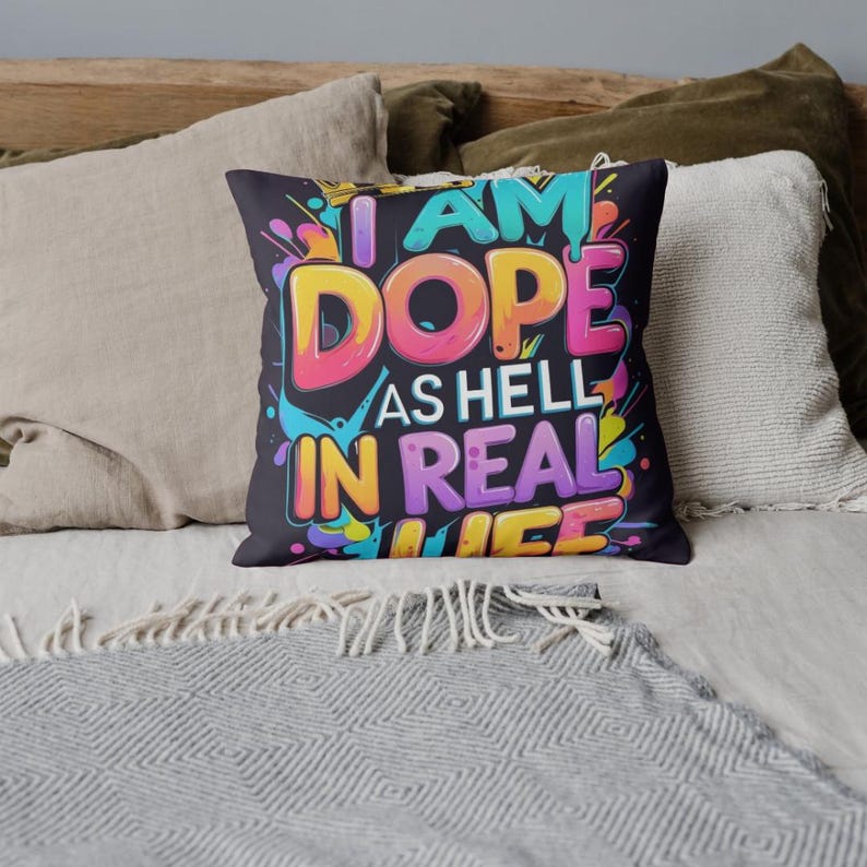 May include: A decorative throw pillow with the text "I AM DOPE AS HELL IN REAL LIFE" in vibrant colors. The pillow has a black background with colorful paint splatter accents, perfect for adding a pop of personality to any space.