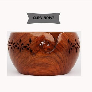 May include: A wooden yarn bowl with a carved design. The bowl is brown and has a hole in the side for the yarn to feed through.