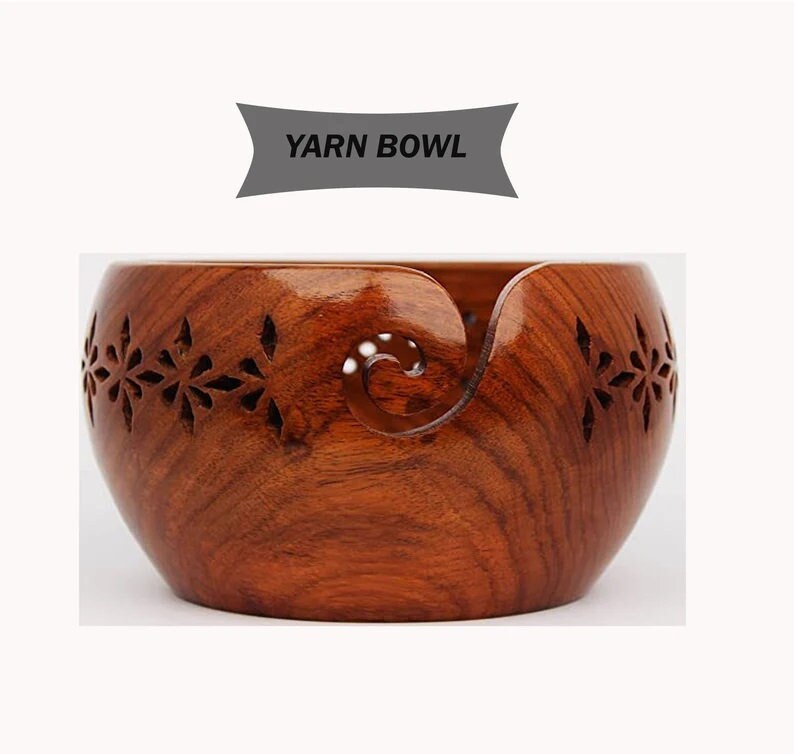 May include: A wooden yarn bowl with a carved design. The bowl is brown and has a hole in the side for the yarn to feed through.