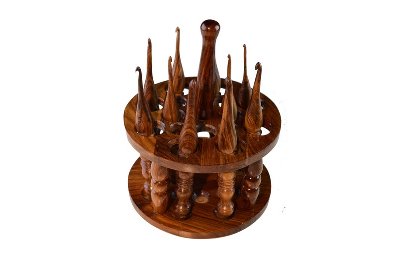 May include: A wooden stand with a rotating base holds a collection of wooden crochet hooks. The hooks are arranged in a circular pattern around the stand, with the tips of the hooks pointing upwards.