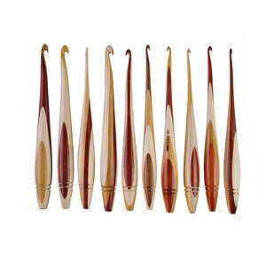 May include: Set of ten wooden crochet hooks with a natural wood and red wood finish. The hooks are all different sizes and are arranged in a row.