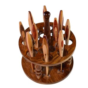 May include: A wooden spinning stand with 18 slots for holding knitting needles. The stand is made of dark wood with a natural wood finish. The needles are made of wood and have a variety of colors and patterns.