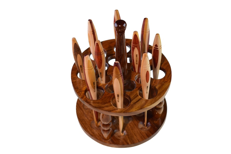 May include: A wooden spinning stand with 18 slots for holding knitting needles. The stand is made of dark wood with a natural wood finish. The needles are made of wood and have a variety of colors and patterns.
