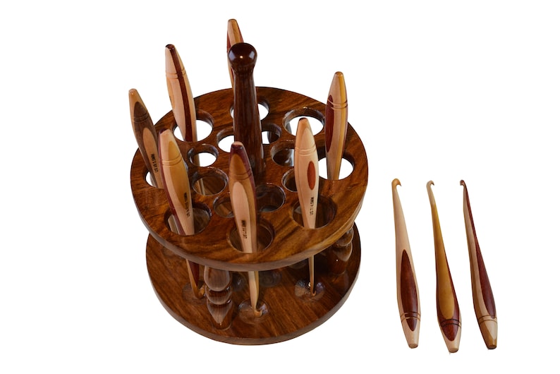 May include: A wooden crochet hook holder with 18 holes and a rotating base. The holder is filled with a variety of wooden crochet hooks. There are also three additional crochet hooks lying on a white surface.