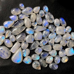 May include: A collection of iridescent moonstone cabochons in various shapes and sizes. The stones are a milky white color with a blue sheen.