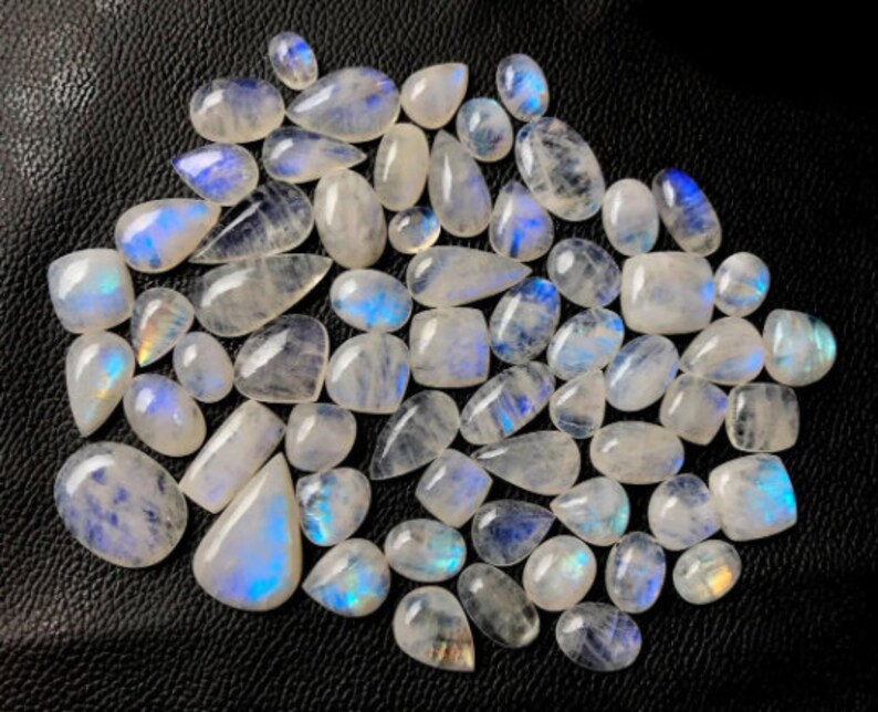 May include: A collection of iridescent moonstone cabochons in various shapes and sizes. The stones are a milky white color with a blue sheen.