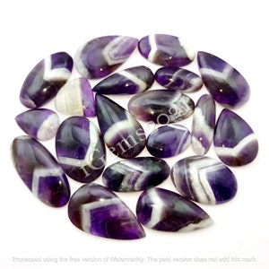 K&ouml;nnte beinhalten: Eine Sammlung von 18 Amethyst-Edelsteinen mit wei&szlig;en und violetten Chevron-Mustern. Die Cabochons haben die Form von Tropfen und liegen lose in einem Haufen.