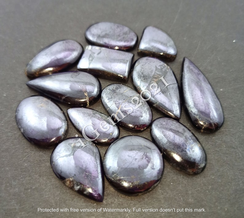 Puede incluir: Una colecci&oacute;n de 13 cabujones de piedras preciosas negras iridiscentes en varias formas, incluyendo ovaladas, en forma de l&aacute;grima y rectangulares. Las piedras tienen un brillo met&aacute;lico y un sutil tono p&uacute;rpura.