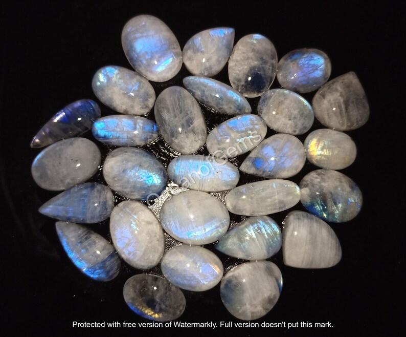 May include: A collection of iridescent moonstone cabochons in various sizes and shapes. The stones are a milky white color with a blue sheen.