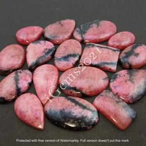 May include: A collection of 15 pink and black gemstone cabochons, some with a teardrop shape, others oval and rectangular. The stones have a mottled appearance with black veins running through them.