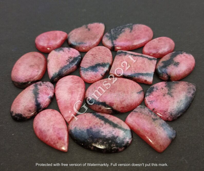 May include: A collection of 15 pink and black gemstone cabochons, some with a teardrop shape, others oval and rectangular. The stones have a mottled appearance with black veins running through them.