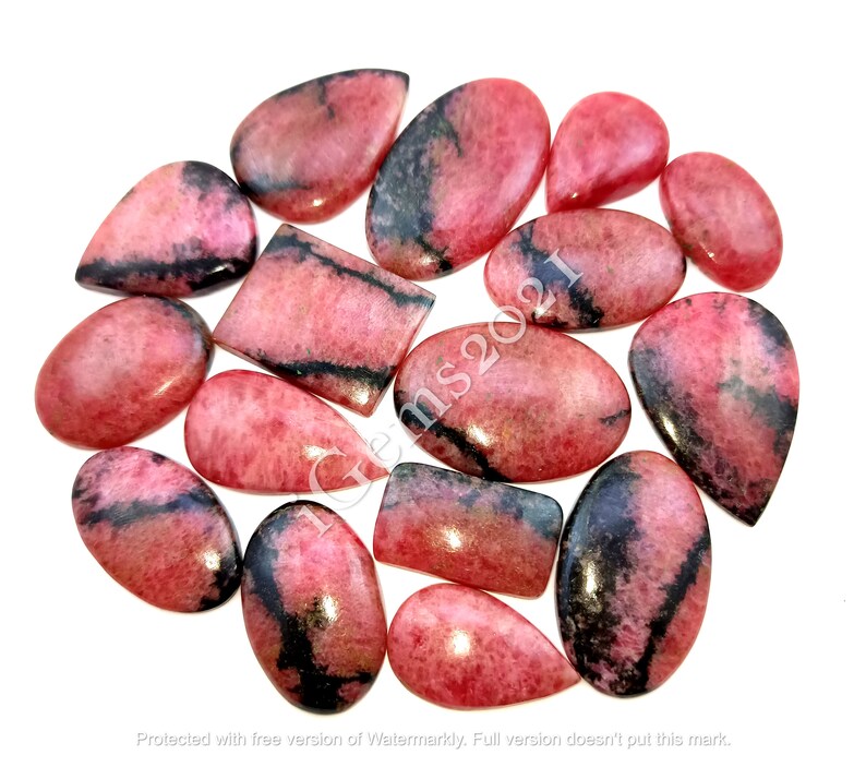 May include: A collection of 15 pink and black gemstone cabochons. The cabochons are various shapes and sizes, including oval, teardrop, and rectangular. The stones have a pink and black marbled pattern.
