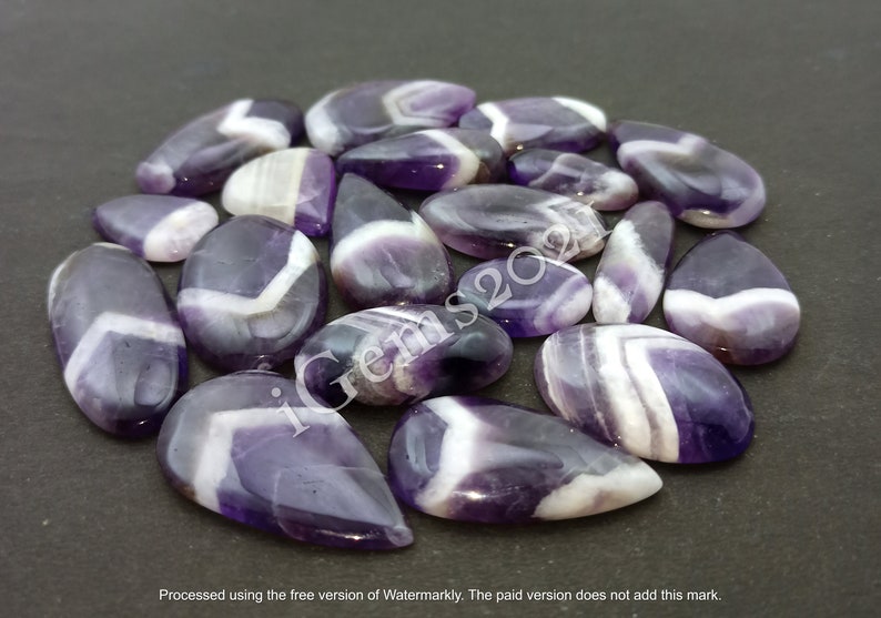 K&ouml;nnte beinhalten: Eine Sammlung von 20 amethystfarbenen Cabochons in Tropfenform mit violetten und wei&szlig;en Streifen.