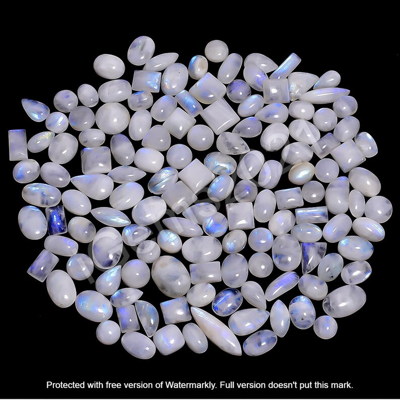 May include: A collection of white moonstone cabochons in various shapes and sizes, including oval, pear, and rectangular. The stones have a iridescent sheen with blue and white colors.