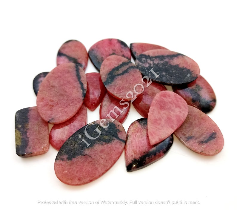 May include: A collection of pink and black gemstone cabochons in various pear and oval shapes. The stones have a striated pattern and are arranged in a pile.
