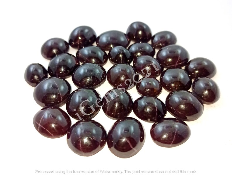 May include: A collection of 20 dark red gemstone cabochons with a star-like pattern. The cabochons are oval shaped and have a smooth, polished surface.
