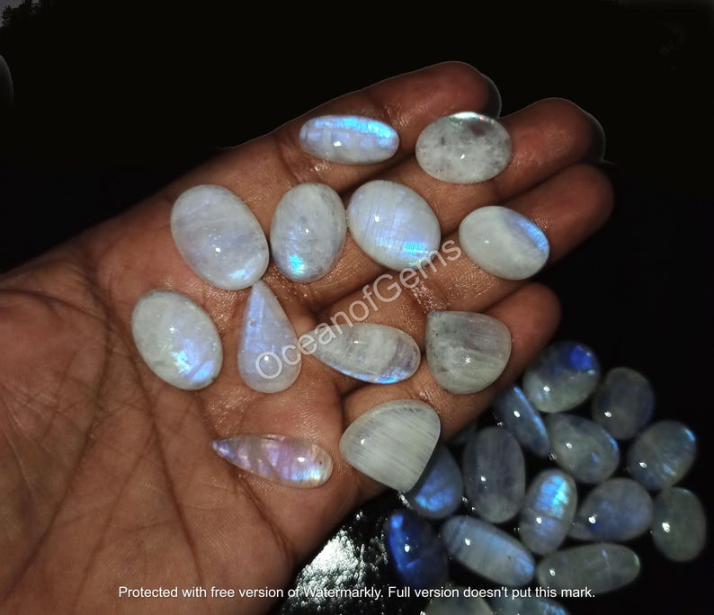 May include: A collection of moonstone cabochons in various sizes and shapes. The stones are a milky white color with a blue iridescent sheen.