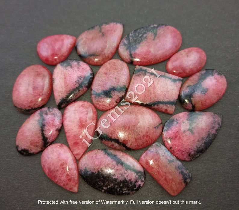 May include: A collection of 15 pink and black gemstone cabochons. The cabochons are various shapes and sizes, including oval, pear, and rectangular. The stones have a smooth, polished finish.