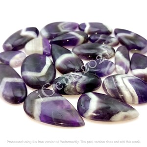 K&ouml;nnte beinhalten: Eine Sammlung von 15 Amethyst-Cabochons mit violetten und wei&szlig;en Streifen. Die Cabochons haben verschiedene Formen und Gr&ouml;&szlig;en und sind alle auf Hochglanz poliert.