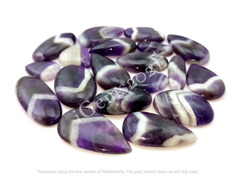 K&ouml;nnte beinhalten: Eine Sammlung von 15 Amethyst-Cabochons mit violetten und wei&szlig;en Streifen. Die Cabochons haben verschiedene Formen und Gr&ouml;&szlig;en und sind alle auf Hochglanz poliert.
