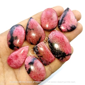 May include: Eight pink and black gemstone cabochons in various shapes, including oval, pear, and rectangle. The stones are polished and have a smooth, glossy finish.