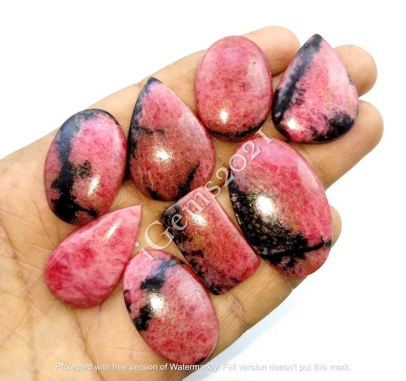 May include: Eight pink and black gemstone cabochons in various shapes, including oval, pear, and rectangle. The stones are polished and have a smooth, glossy finish.