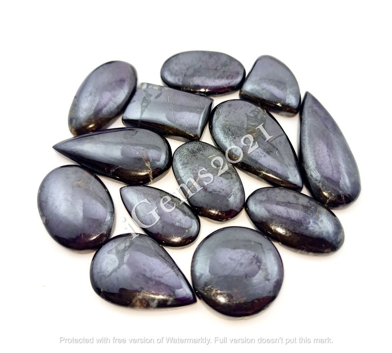 Puede incluir: Una colecci&oacute;n de 12 cabujones de piedras preciosas negras iridiscentes en varias formas, incluyendo ovalada, l&aacute;grima y rectangular. Las piedras tienen un acabado brillante y met&aacute;lico.