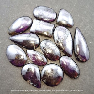 Puede incluir: Una colecci&oacute;n de 12 cabujones de piedras preciosas iridiscentes en tonos de p&uacute;rpura y plata. Las piedras son de varias formas y tama&ntilde;os, incluyendo l&aacute;grima, ovalado y rectangular.