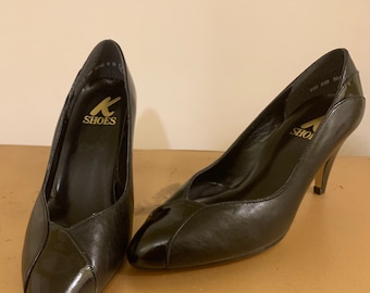 May include: A pair of black leather high-heeled pumps with a pointed toe. The shoes have a patent leather cap toe and the brand name "K SHOES" is printed on the insole.