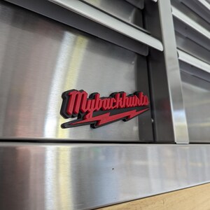 May include: A red and black metal logo with the text "Myrackhurts" and a lightning bolt. The logo is attached to a stainless steel surface.