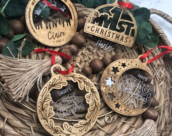 May include: Four wooden Christmas ornaments with a clear acrylic insert. The ornaments are decorated with the words "My First Christmas", "1st Christmas", "Baby's First Christmas", and "Emory's First Christmas". Each ornament has a red ribbon and a brown tassel.