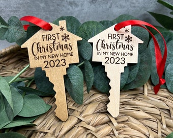 May include: Two wooden key-shaped ornaments with a house design. Each ornament has a red ribbon and the text "FIRST Christmas IN MY NEW HOME 2023".