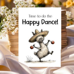 May include: A greeting card with the text "Time to do the Happy Dance!" features a cartoon llama wearing a sombrero and holding maracas. The llama is dancing on a white background. The card is surrounded by flowers and a stack of books.