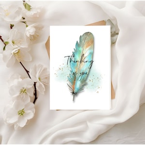 May include: A white card with a blue and brown watercolor feather and the text "Thinking of you" in black script.