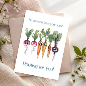 May include: A greeting card with a watercolor illustration of smiling radishes, carrots, and beets. The card reads "No one can beet your spirit!" and "Rooting for you!" in teal text. The card is on a neutral background.