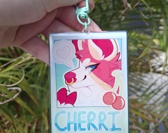 Op de afbeelding: Een heldere acryl sleutelhanger met een cartoon wolf met roze en witte vacht, blauwe ogen en een gouden neusring. Het ontwerp bevat een hartvormige tekstballon, kersen en de naam "CHERRI" in blauwe letters.
