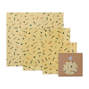 May include: Set of four beeswax food wraps in various sizes with a geometric pattern of triangles, lines, and dots in shades of brown, green, and orange on a light yellow background. The wraps are packaged in a brown paper envelope.