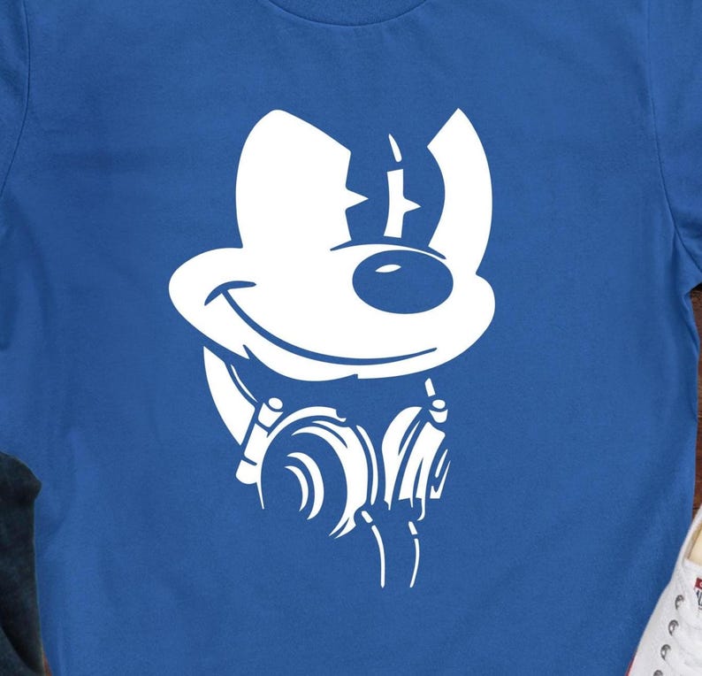 May include: A blue t-shirt with a white graphic of a cartoon mouse head wearing headphones. The mouse has a smiling face and large ears. The headphones are depicted with curved lines.