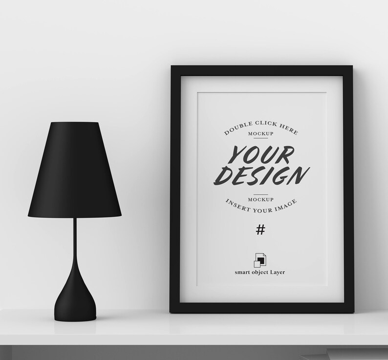 May include: A black framed print with the text "YOUR DESIGN" and a black lamp with a conical shade. The lamp has a slender stem and a rounded base. The print is a mockup with instructions to insert an image.