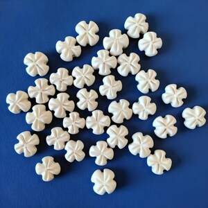 Può includere: Una collezione di perline di ceramica bianca a forma di fiore su uno sfondo blu. Le perline sono tutte della stessa dimensione e forma, e sono disposte in uno schema casuale.