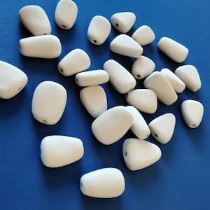May include: A collection of white, smooth, oval-shaped stones with a hole drilled through the centre. The stones are arranged on a blue background.